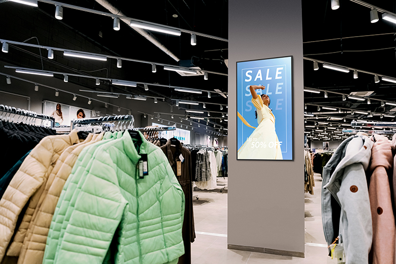 Portrait digital signage screen on a pillar in a clothing shop displaying a sale promotion